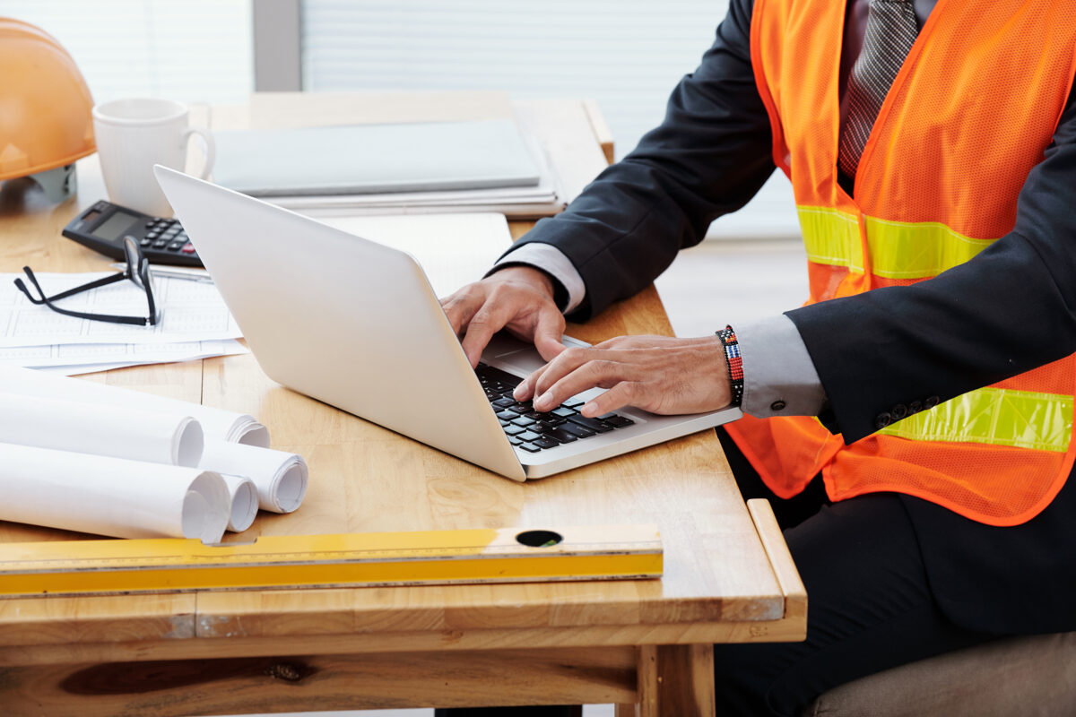 unrecognizable-man-neon-safety-vest-business-suit-sitting-desk-using-laptop.jpg